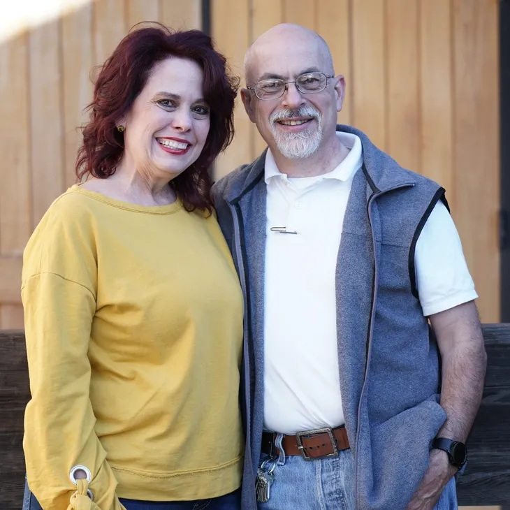 Smiling couple posing outdoors by wooden fence
