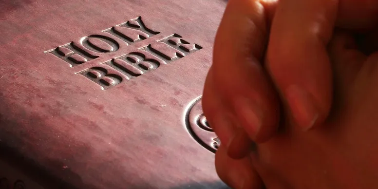 Hands praying over a Bible